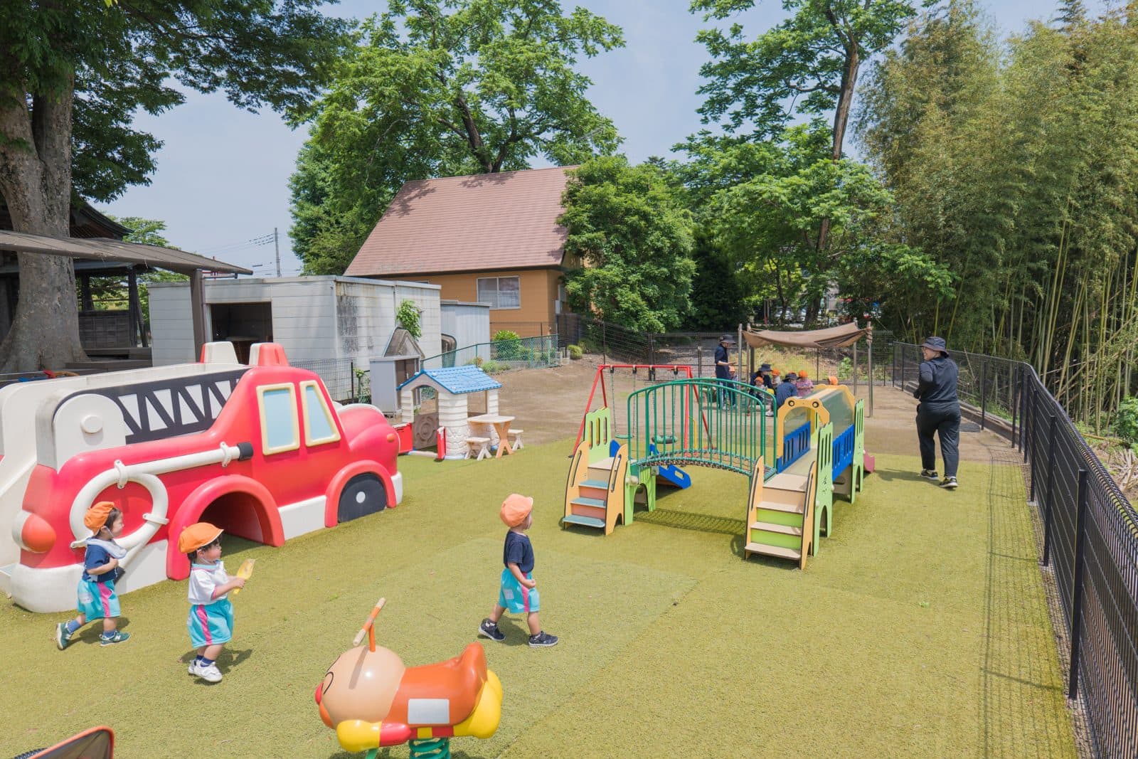 人工芝のベビーガーデン全景。消防車の遊具やアスレチックであそぶ小さな子どもたち