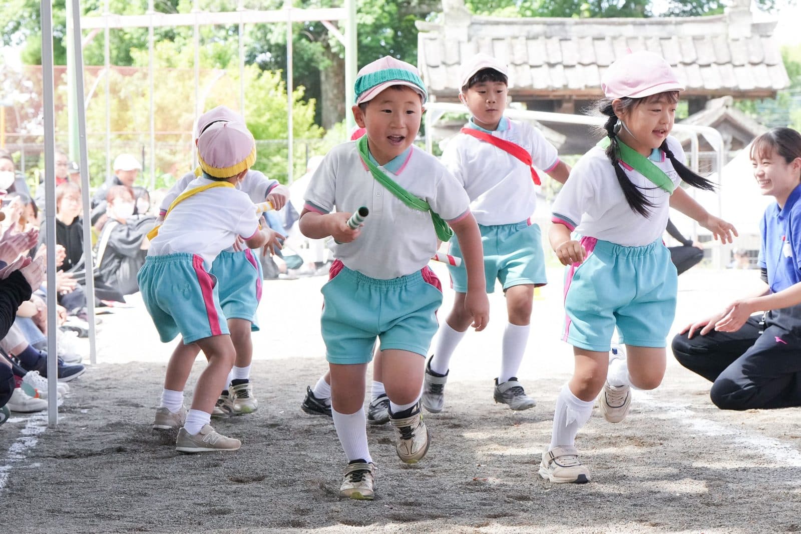 園庭での運動会で、バトンを持ってリレーを走る子どもたち