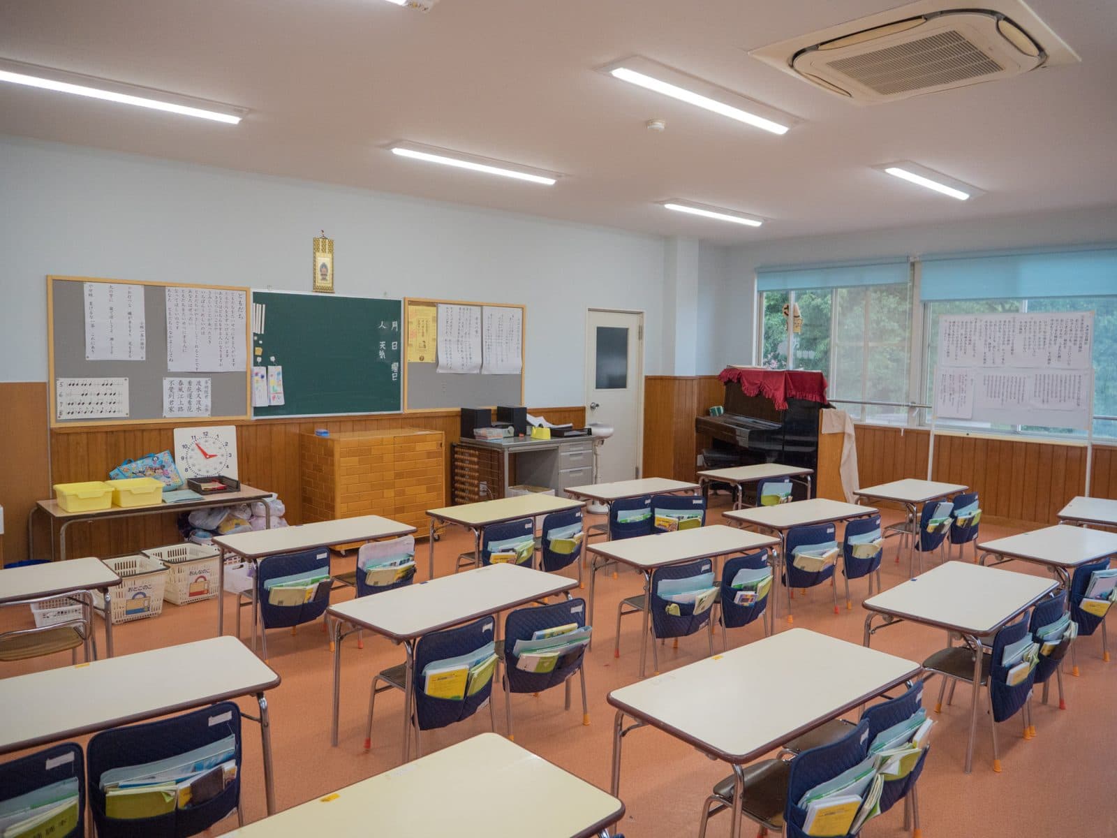 机といすが並ぶ3〜5歳児の保育室。ピアノと黒板があります