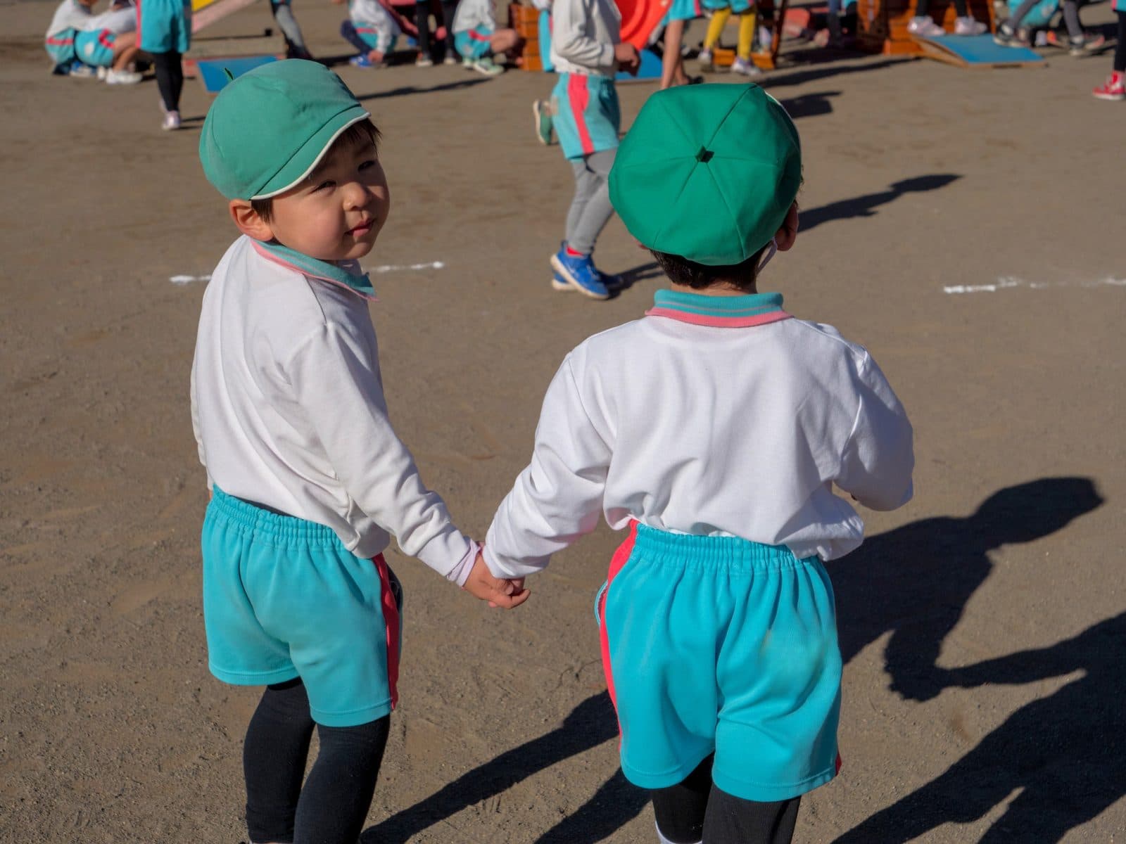 園庭で手をつなぎ、振り返ってほほえむ2人の園児