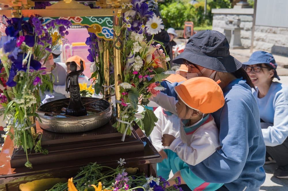 花まつりで、花で飾った花御堂の誕生仏に手を伸ばす園児と保護者