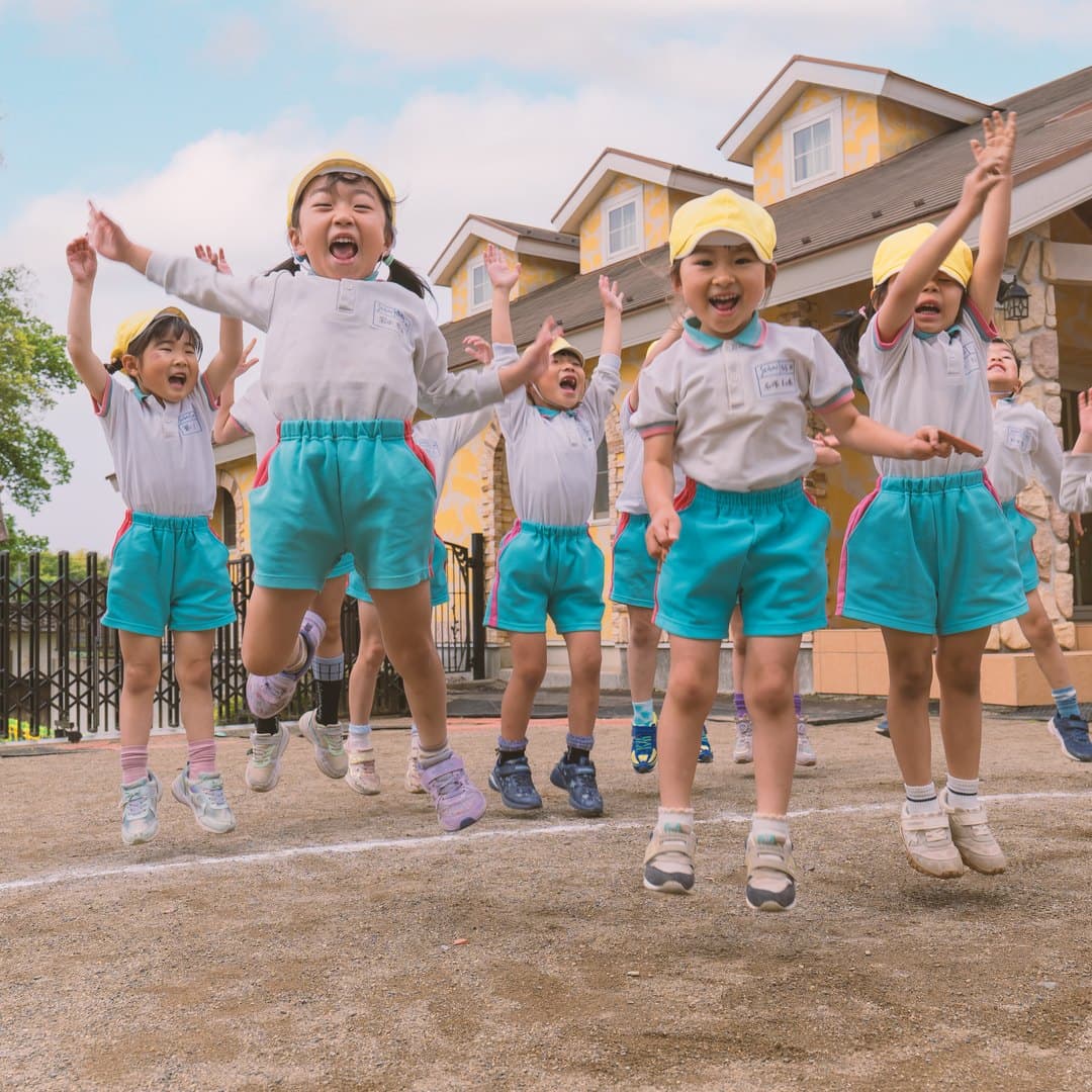 広い園庭で子どもたちが空に向かって一斉にジャンプしている様子