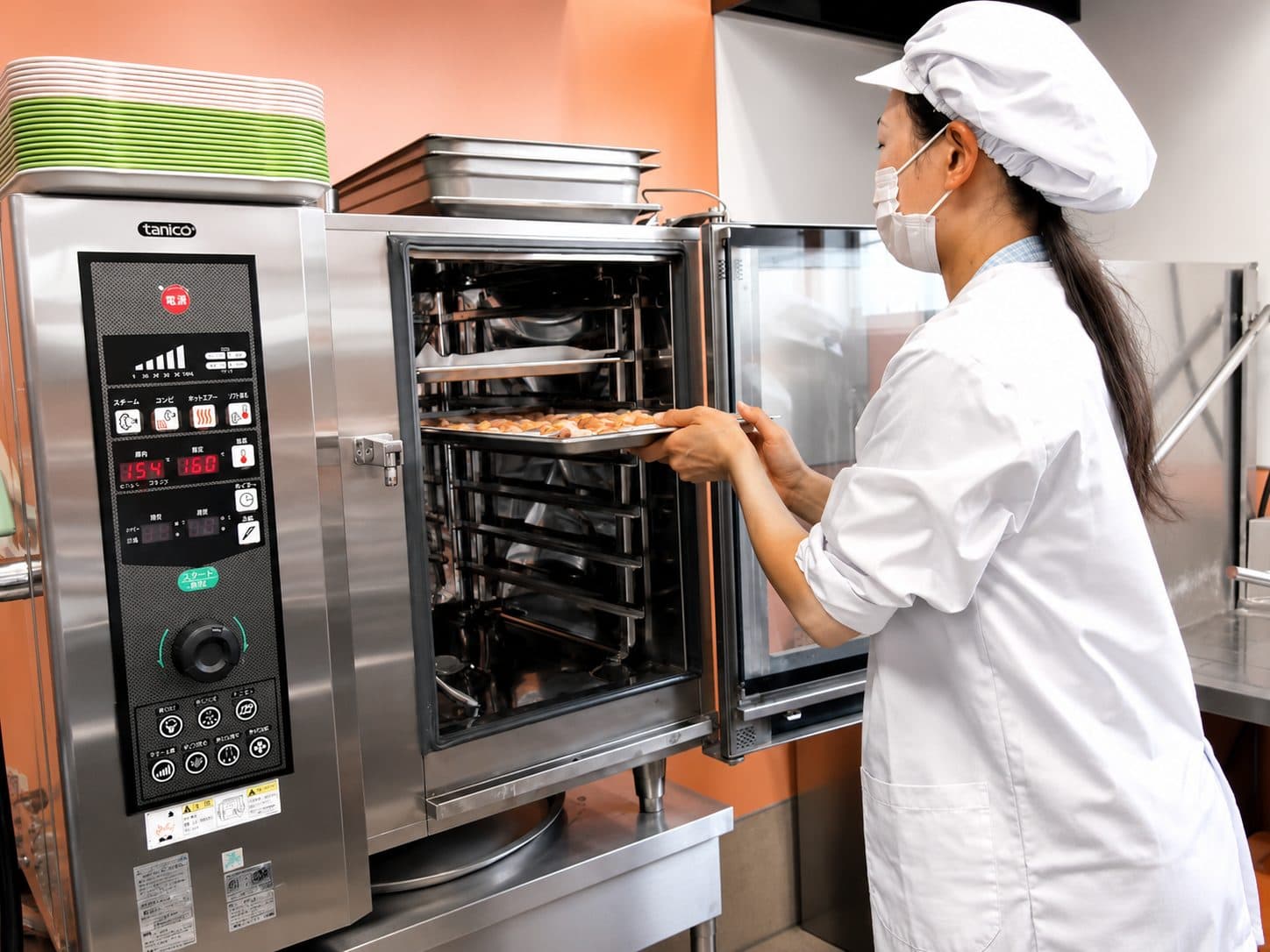 自園厨房で、調理員がスチームオーブンから焼きたての料理を取り出す様子