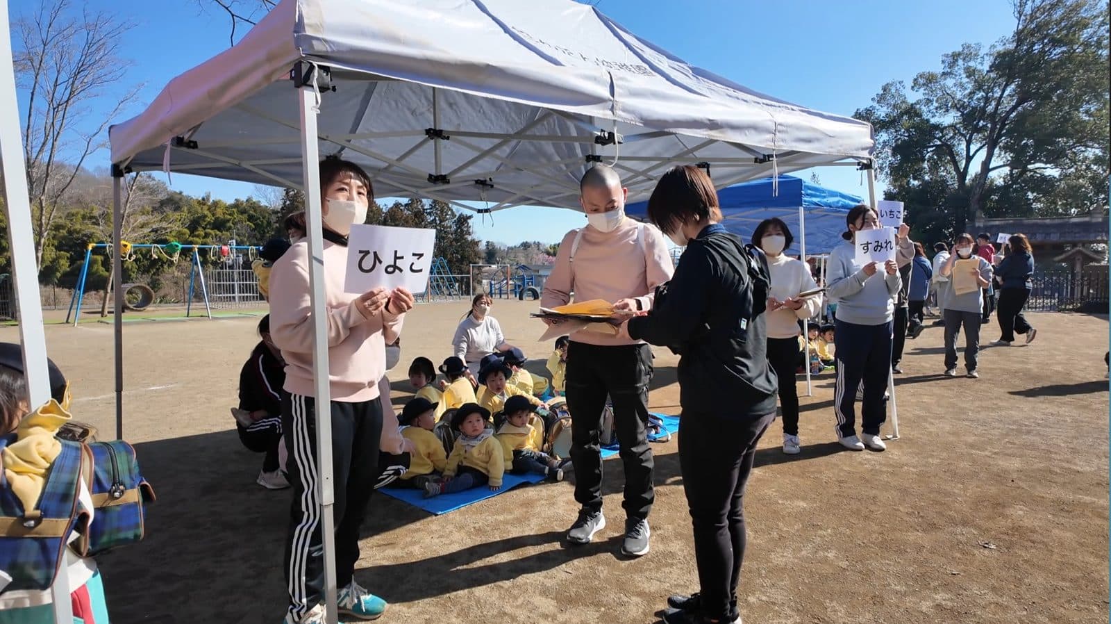 引き渡し訓練で、クラス名のプラカードを掲げて保護者にお子さまを引き渡す先生たち