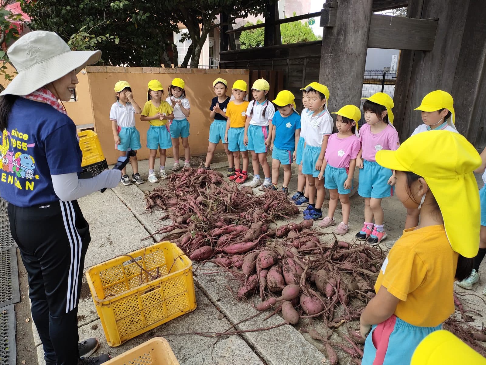 収穫したさつまいもの山の前で、子どもたちに話をする園長