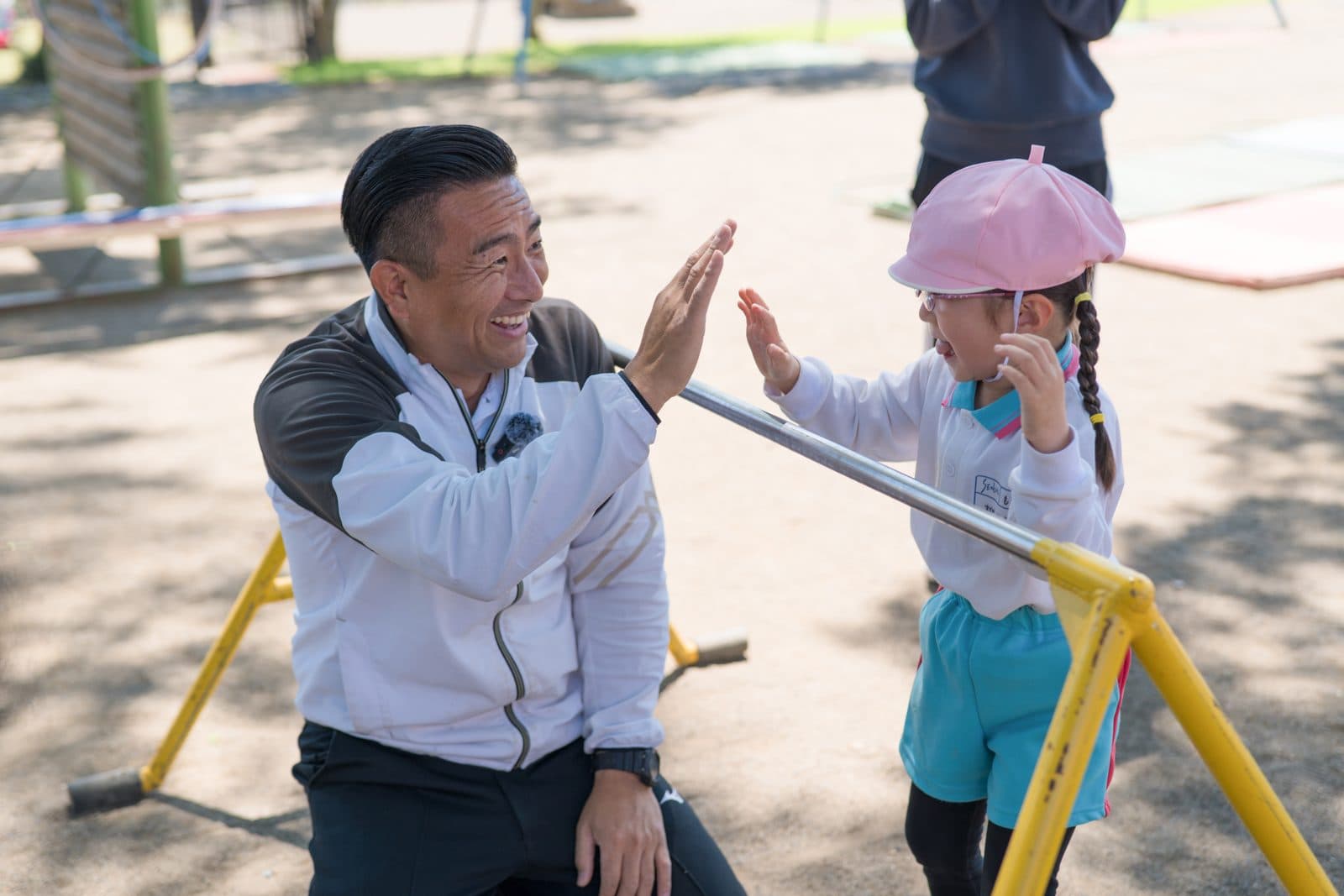 鉄棒ごしに、体操の先生と園児が笑顔でハイタッチする様子