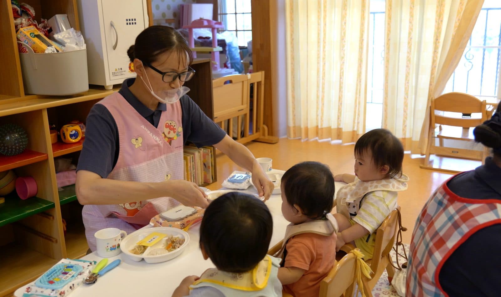 エプロン姿で0歳児の給食を介助する先生