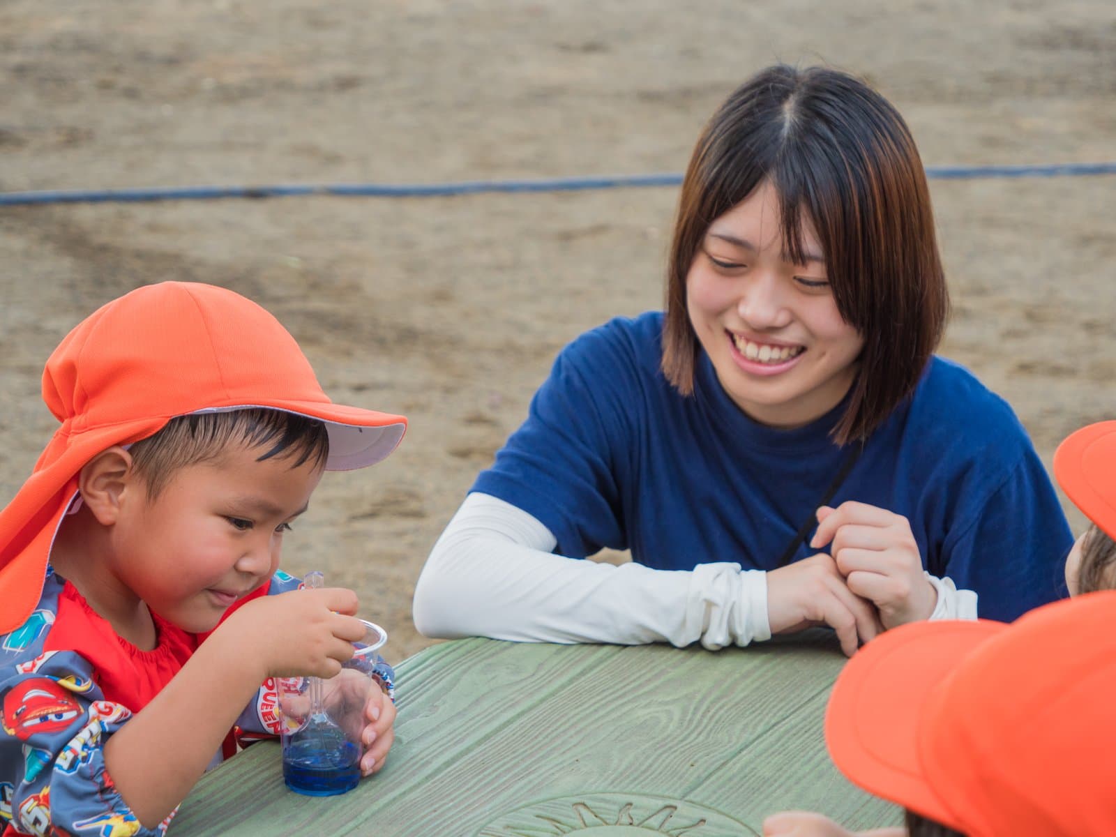 2歳児の色水あそびで、夢中になる子どもの手元をいっしょにのぞきこみ、笑顔で見守る先生