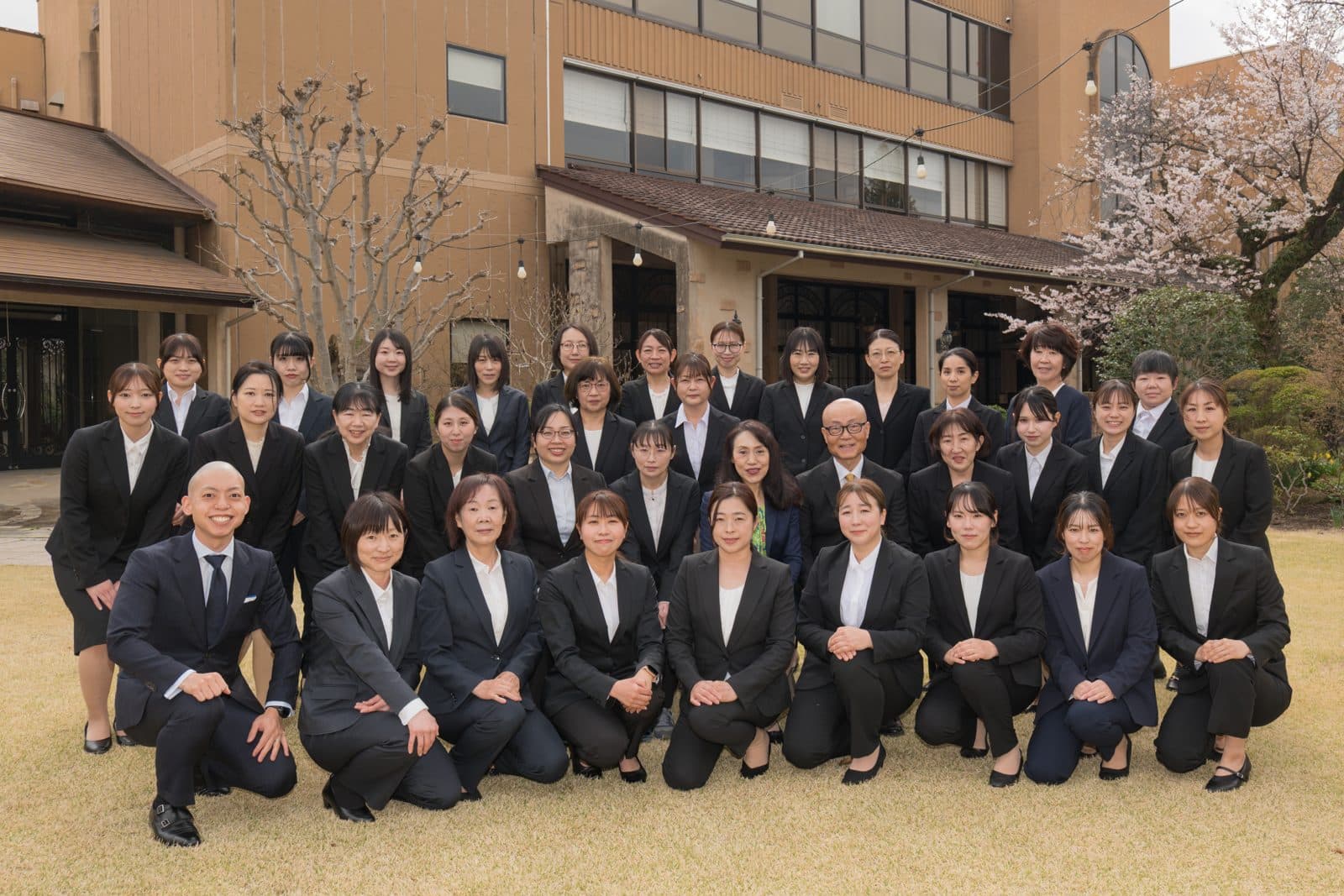 桜の咲く園庭で撮影した、令和8年度の職員集合写真